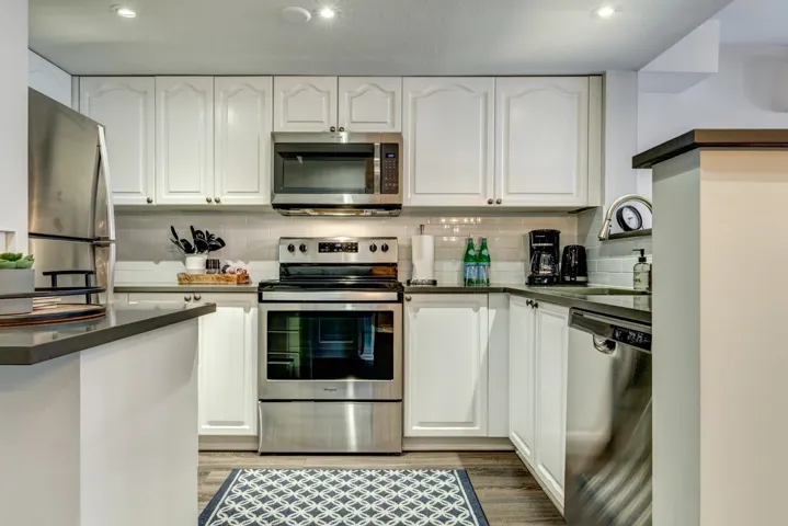 Kitchen featuring appliances with stainless steel finishes, dark countertops, white cabinetry, and tasteful backsplash