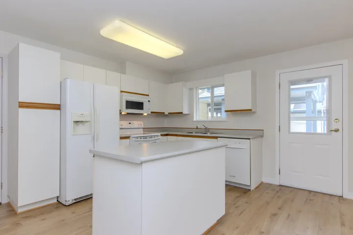 Kitchen with white cabinets, white appliances, light wood finished floors, and light countertops