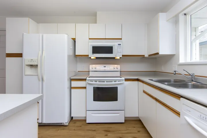 Kitchen featuring white cabinets, white appliances, light wood-type flooring, and light countertops