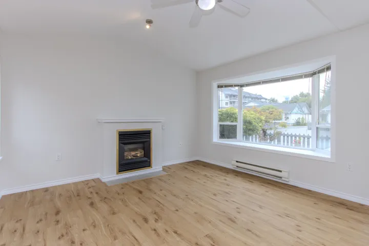 Unfurnished living room with baseboard heating, a glass covered fireplace, lofted ceiling, light wood-style flooring, and ceiling fan