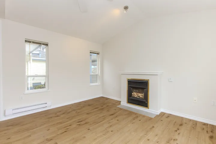 Unfurnished living room featuring lofted ceiling, baseboard heating, wood finished floors, and a fireplace with flush hearth