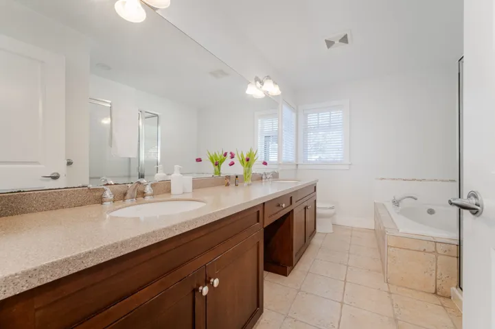 Full bathroom with a bath, double vanity, a stall shower, toilet, and baseboards