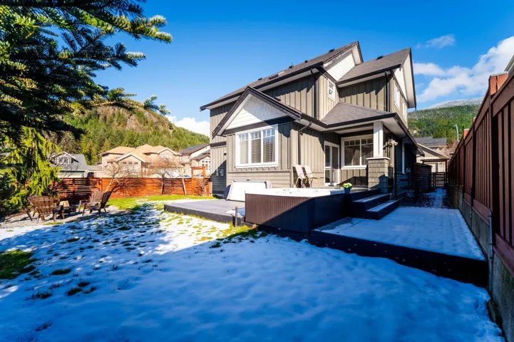 Rear view of property featuring board and batten siding, a deck with mountain view, fence, a shingled roof, and a fire pit