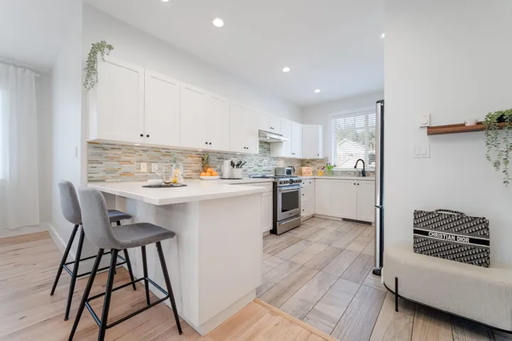 Kitchen with appliances with stainless steel finishes, under cabinet range hood, white cabinetry, a breakfast bar, and recessed lighting