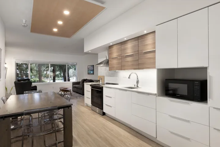 Kitchen featuring modern cabinets, open floor plan, black appliances, wall chimney range hood, and light wood-type flooring