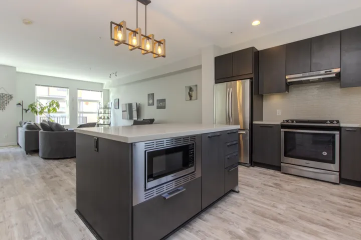 Kitchen with decorative light fixtures, stainless steel appliances, backsplash, open floor plan, and under cabinet range hood