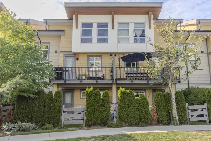 View of rear of building with fenced yard, access to landscaped courtyard and private balcony off the kitchen
