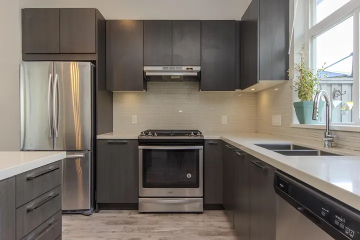 Kitchen with appliances with stainless steel finishes, modern cabinets, backsplash, under cabinet range hood, and light stone counters