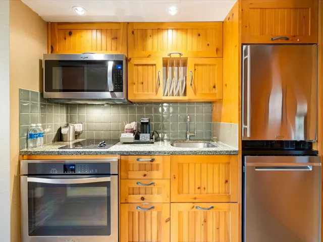 Kitchen featuring appliances with stainless steel finishes, decorative backsplash, light stone countertops, recessed lighting, and brown cabinets