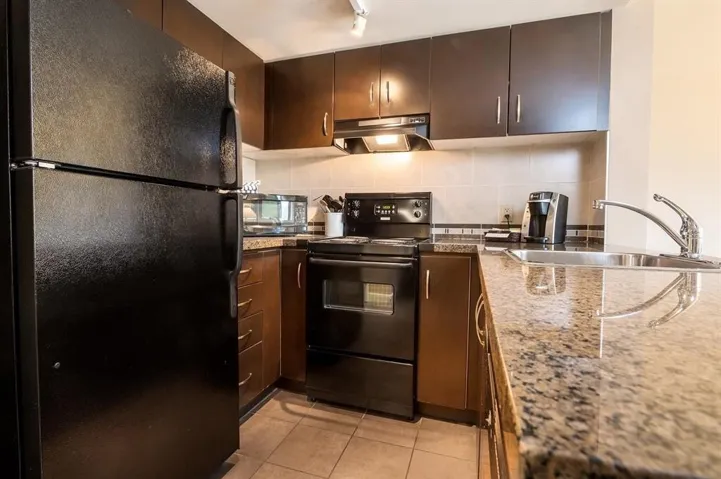 Kitchen with black appliances, under cabinet range hood, light tile patterned floors, backsplash, and track lighting