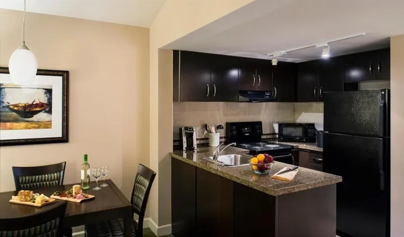 Kitchen with black appliances, rail lighting, a peninsula, dark cabinetry, and tasteful backsplash