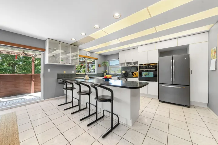 Kitchen featuring a large central island with seating, white shaker-style cabinetry, integrated wall oven, and a double-door refrigerator