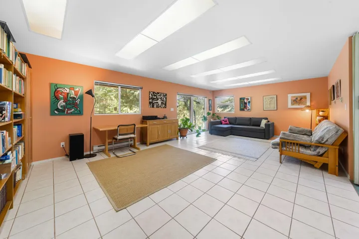 Spacious interior room featuring white tile flooring, peach-toned walls, and multiple rectangular ceiling light panels
