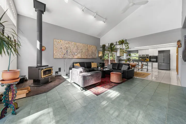 Spacious living area featuring a vaulted ceiling and a freestanding wood-burning stove on a dark tile hearth