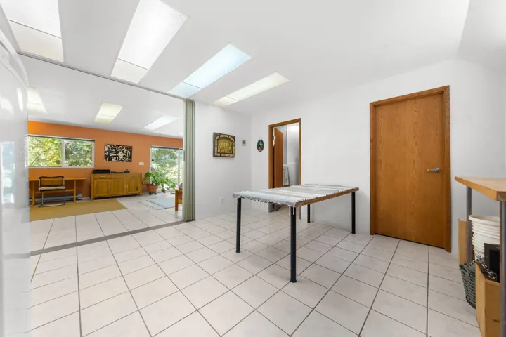 Bright interior space featuring white tile flooring, multiple skylights, and a partition opening to a room with broad windows