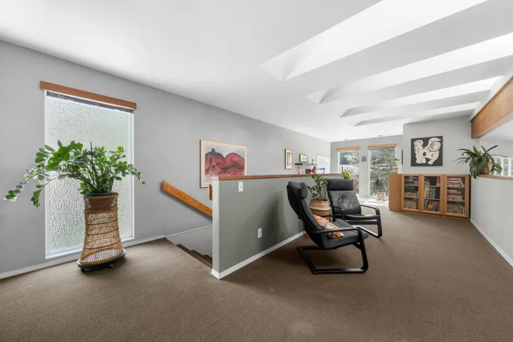Carpeted loft area featuring a textured window, wood staircase railing, and a built-in wood cabinet with glass-paneled doors