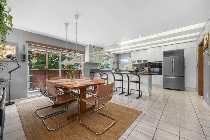 Open-concept kitchen and dining area featuring light-toned tile flooring, white cabinetry, integrated stainless steel appliances, a kitchen island with bar seating, and a dining area with pendant lighting