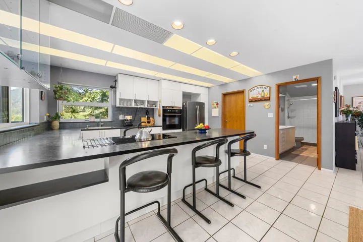 Kitchen featuring a large island with dark countertops, white cabinetry, integrated oven, and tile flooring