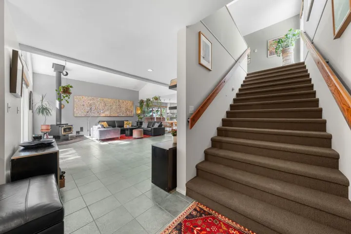 Carpeted staircase with wood handrails, light gray wall color, and adjacent tiled flooring