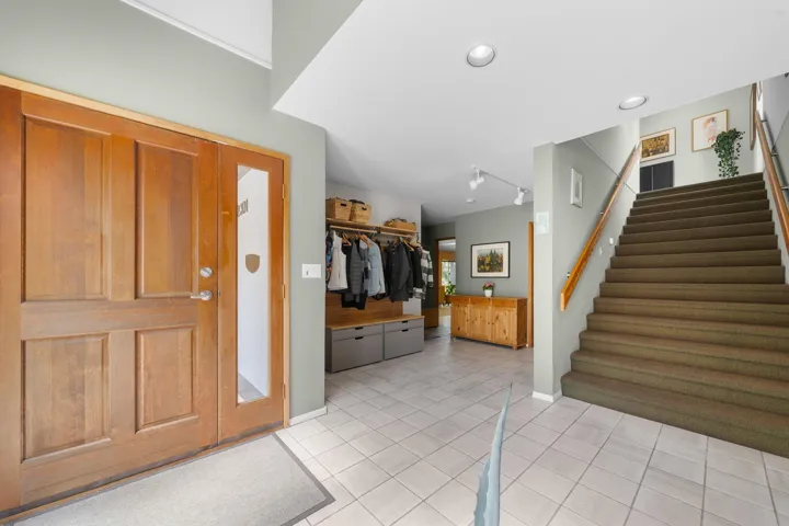 Entryway featuring a natural wood-finish door with sidelight, tile flooring, built-in storage, recessed lighting, and a staircase with a wood-finish handrail