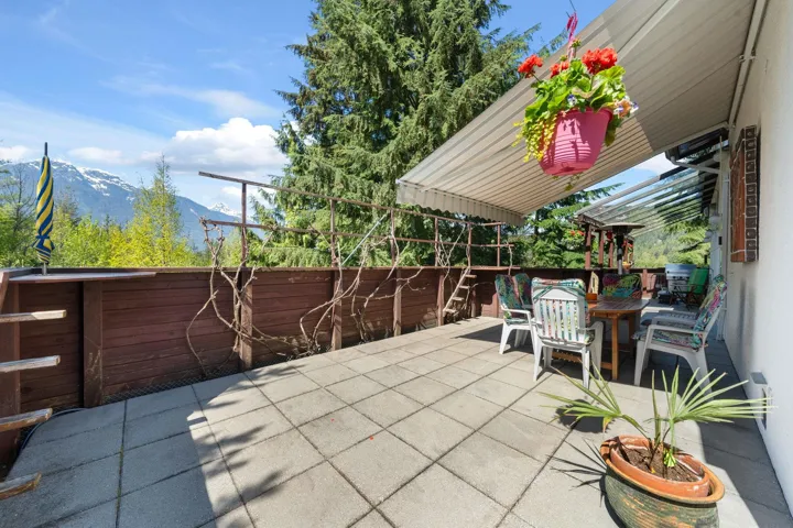 Expansive outdoor patio featuring square paver flooring, a retractable striped awning, and a brown wood-paneled privacy fence