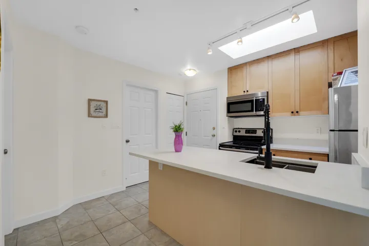 Kitchen featuring light-finish cabinetry, a white countertop peninsula, stainless steel appliances, a skylight, and a matte black gooseneck faucet