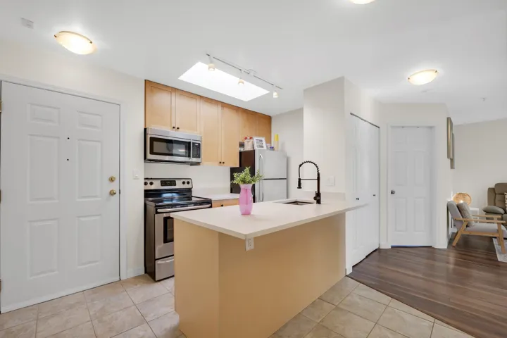 Kitchen featuring light-finish cabinetry, stainless steel appliances, a peninsula with a matte black high-arc faucet, a skylight, and tile flooring