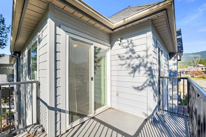 Private balcony featuring light gray horizontal lap siding, sliding glass doors, and a black metal railing