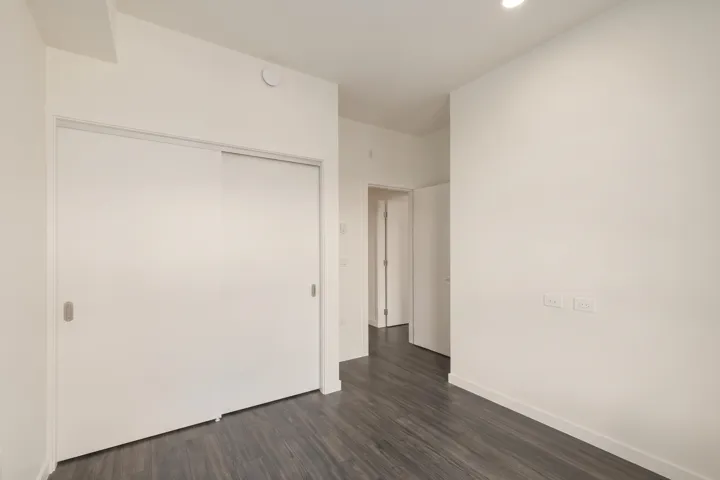 Interior space featuring dark wood-finish flooring, white walls, and a built-in sliding-door closet with metallic recessed hardware