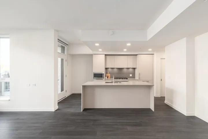 Modern kitchen featuring light cabinetry, an integrated microwave, a center island with sink, and dark wood-finish flooring