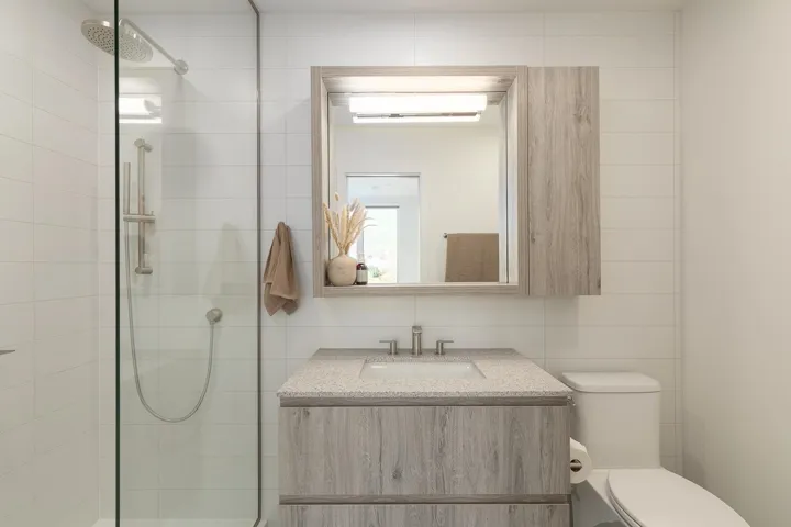 Wood-finish vanity with a stone-composite countertop, integrated medicine cabinet, walk-in shower with a glass enclosure, and rainfall showerhead