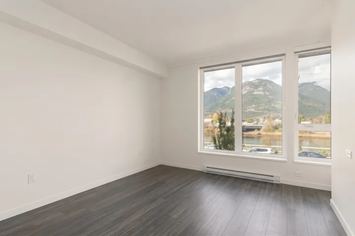 Neutral-toned interior featuring wood-finish flooring, oversized windows, and expansive mountain and water scenery
