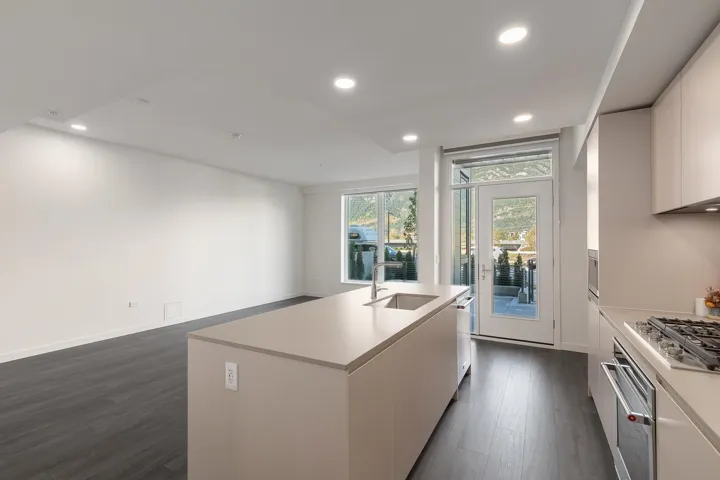 Open-concept living area featuring wood-finish flooring, a kitchen island with an undermount sink, recessed lighting, and a glass-paneled exterior door