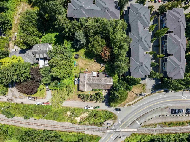Aerial perspective showcasing a residential property with surrounding mature trees, a multi-pitched roof, and a visible backyard area