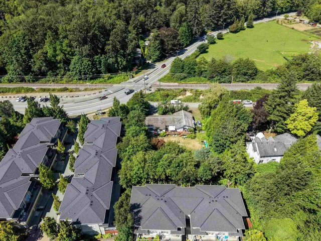 Aerial perspective showcasing a residential development with dark gray roofs, extensive surrounding greenery, and a highway nearby