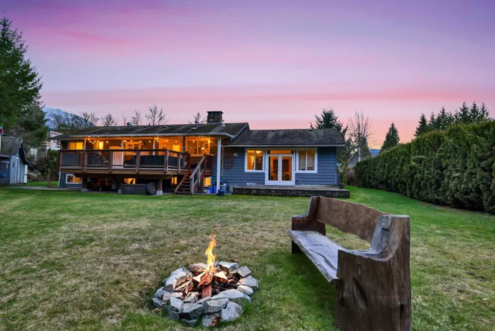 Back of property at dusk featuring a yard, a wooden deck, a chimney, and an outdoor fire pit