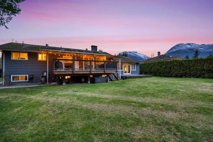 Rear view of property with a deck with mountain view, a yard, and a chimney