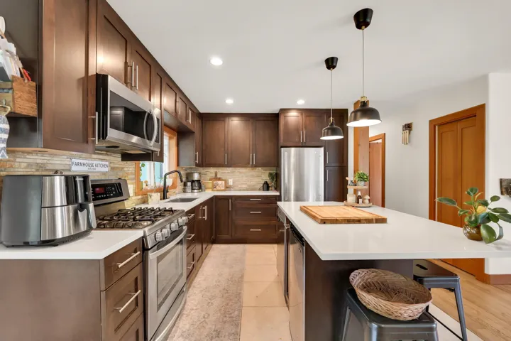 Kitchen featuring stainless steel appliances, a kitchen breakfast bar, dark wood finish cabinets, hanging light fixtures, and a center island