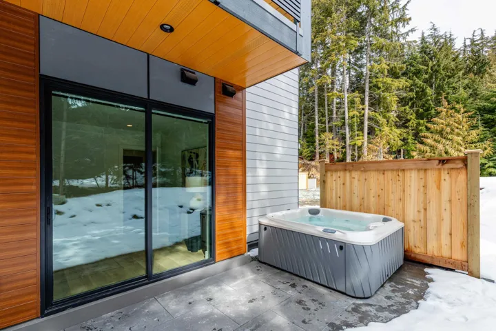 Contemporary residential buildings set amidst a coniferous forest, featuring snow-dusted ground and surrounding mountain peaks