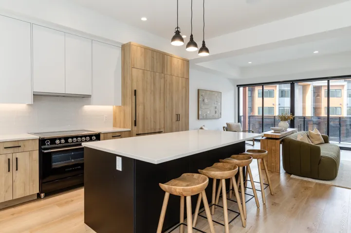 Kitchen with light wood-type flooring, black range with induction stovetop, Fisher Paykel appliances, open floor plan, and a breakfast bar.