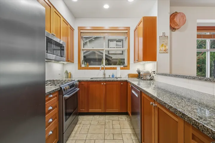 Kitchen with stainless steel appliances, light stone finish flooring, dark stone counters, recessed lighting, and wood finish cabinets
