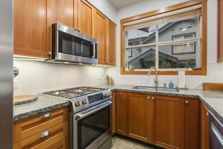 Kitchen featuring stainless steel appliances, wood finish cabinetry, and light stone countertops