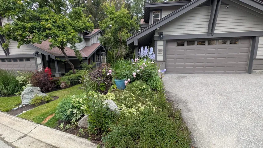 Contemporary-style home featuring a two-car garage with panel detailing, a paved driveway, and an established front garden with diverse plantings