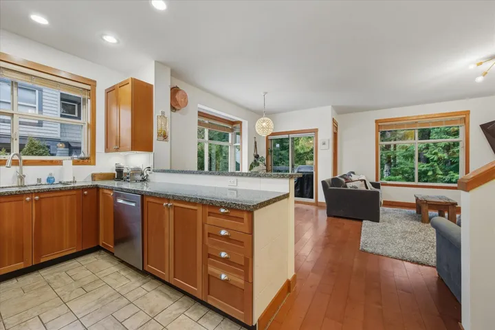 Kitchen with dark stone counters, a peninsula, open floor plan, stainless steel dishwasher, and light wood-style floors