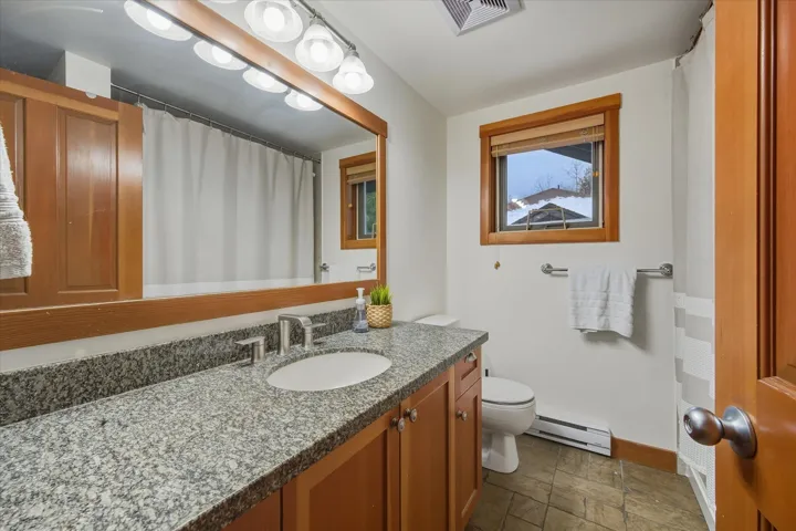 Full bath with curtained shower, vanity, and baseboard heating