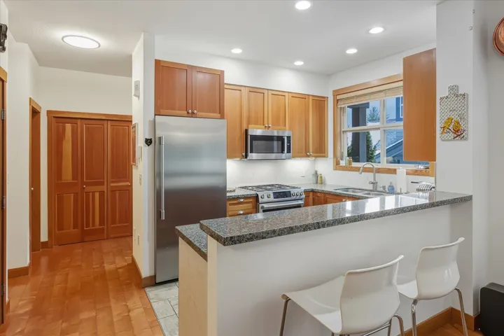 Kitchen featuring stainless steel appliances, a peninsula, a kitchen bar, dark stone countertops, and light wood finished floors
