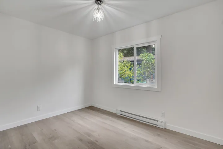 Empty room featuring a baseboard radiator, light wood finished floors, and a chandelier
