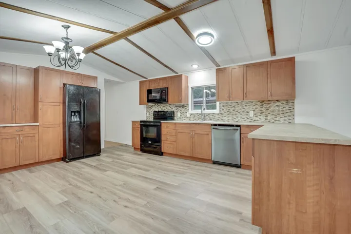 Kitchen with light countertops, black appliances, backsplash, light wood-style flooring, and pendant lighting