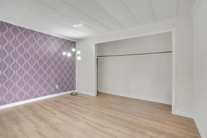 Unfurnished bedroom with wallpapered walls, light wood finished floors, and an accent wall