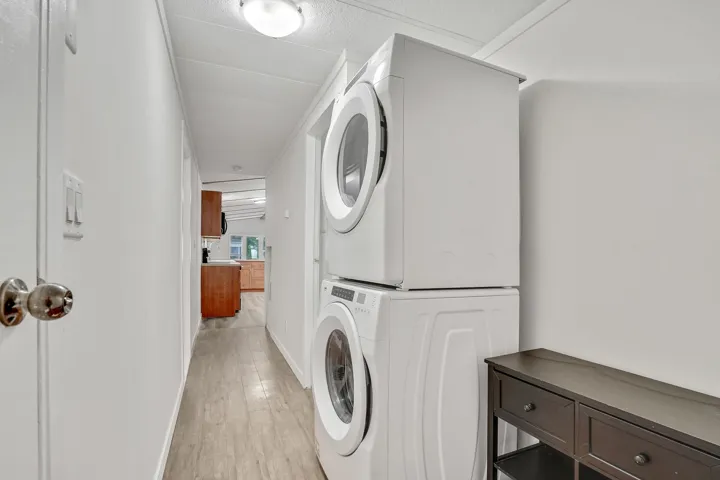 Washroom with light wood-type flooring and stacked washing machine and dryer